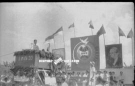 Tampak seorang sedang berada di panggung untuk berorasi dengan latar belakang foto tokoh Karl Mar...