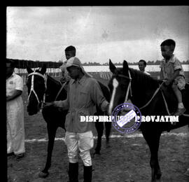 Seorang joki sedang memegang tali kendali 2 ekor kuda yang dinaiki anak-anak dalam lomba pacuan (...