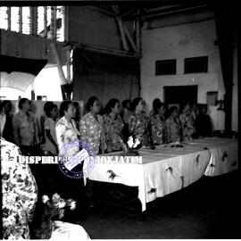 Para hadiri sedang berdiri dalam sebuah acara pertemuan yang merupakan gabungan organisasi wanita...