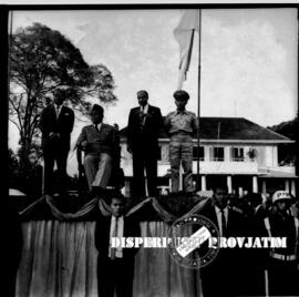 Presiden Sukarno sedang duduk di atas panggung didampingi tiga orang dalam peringatan peringatan ...