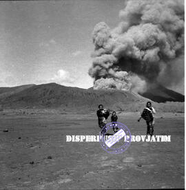 Tiga orang perempuan tengah berjalan dilautan pasir dengan latar belakang kepulan asap gunung bro...